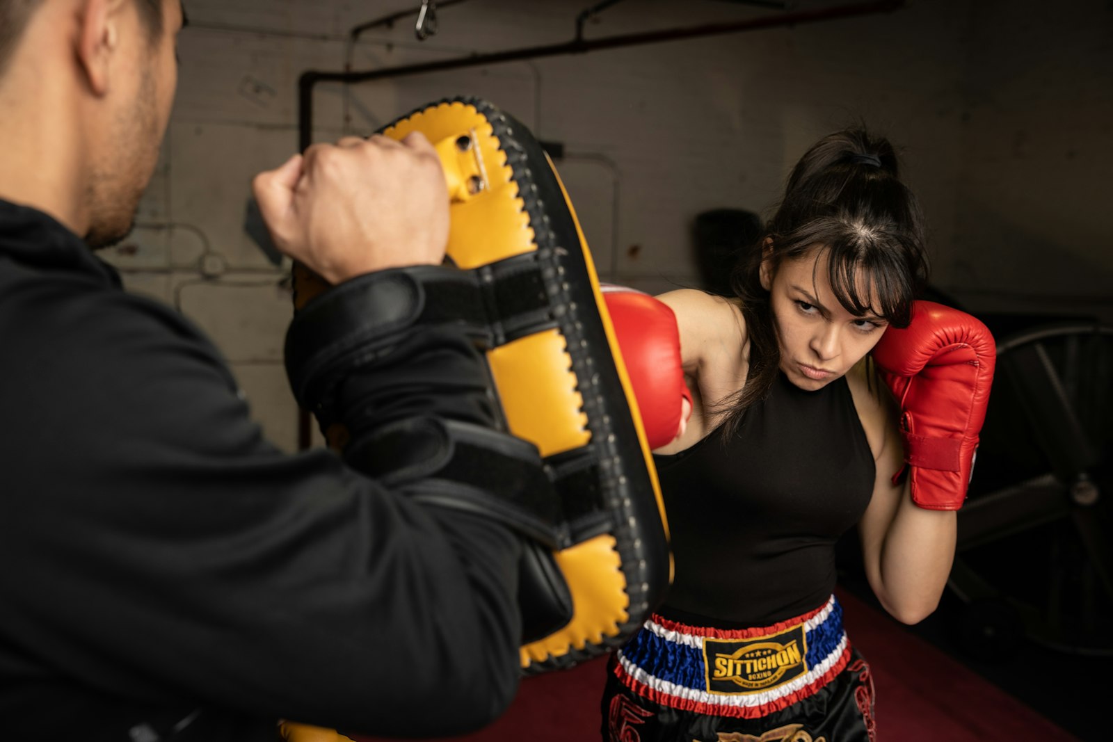 A coach holds a pad while a client in red gloves throws a punch.